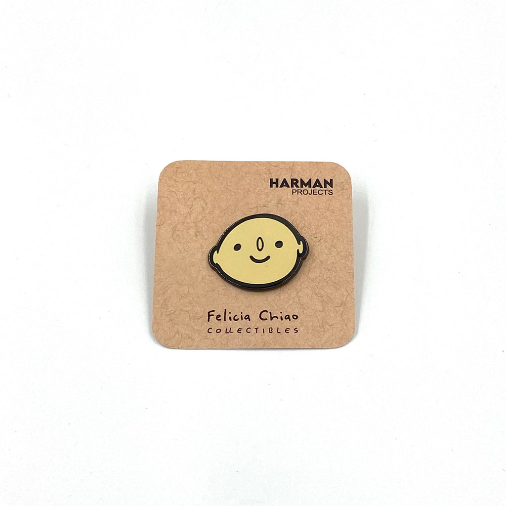 Photo of enamel pin of a smiling face on a natural brown backer on a white background